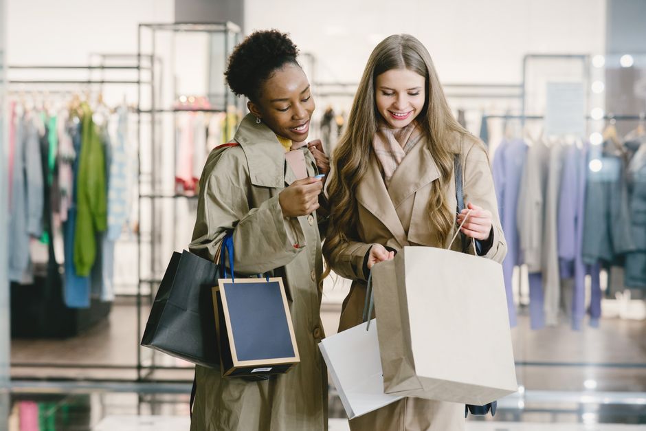 Smiling women shopping together with paper bags in a stylish clothing store.